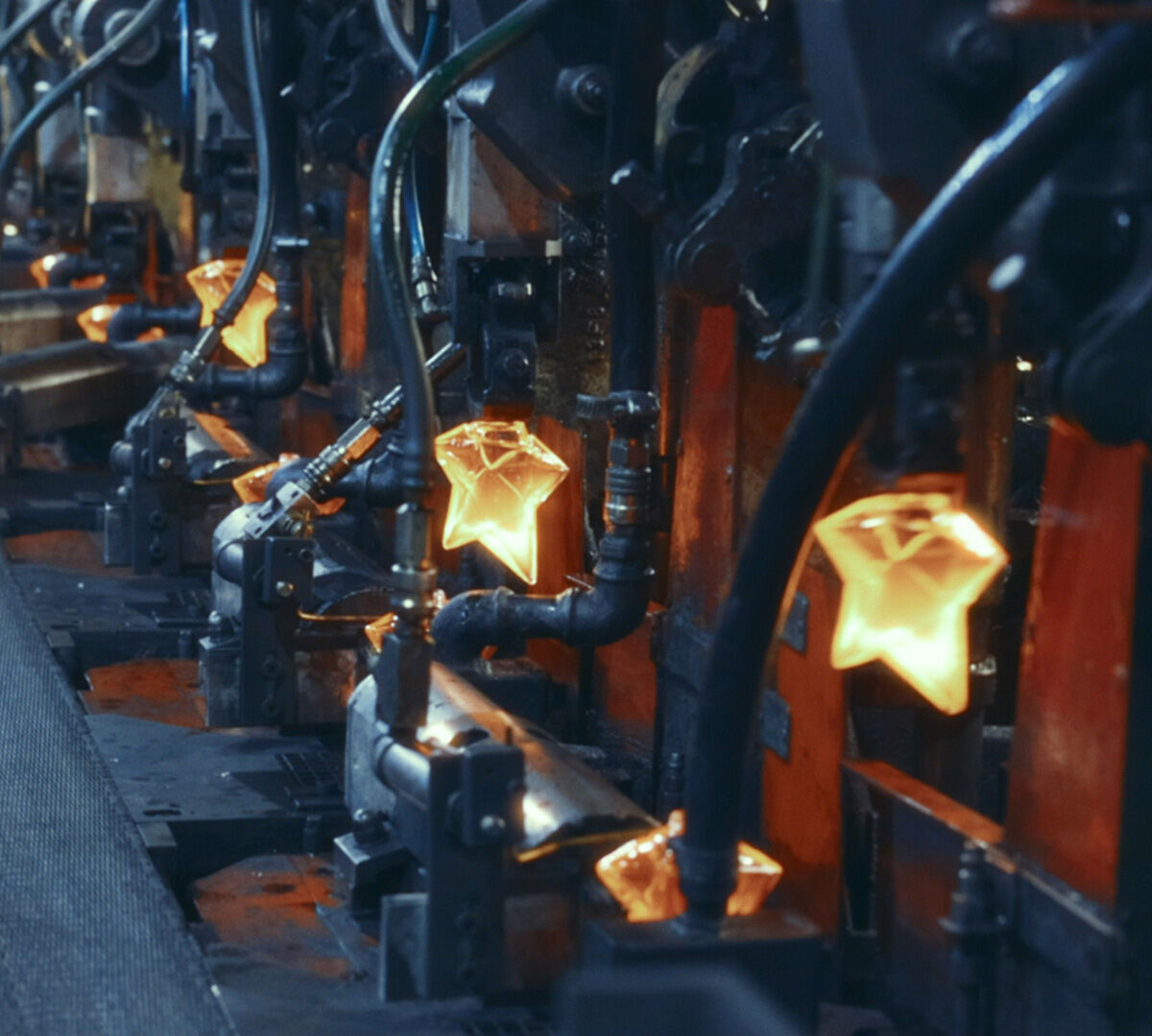 fabrication de plusieurs objets en verre en forme d'etoile, aux reflets orange et jaune, sur une chaine de montage.