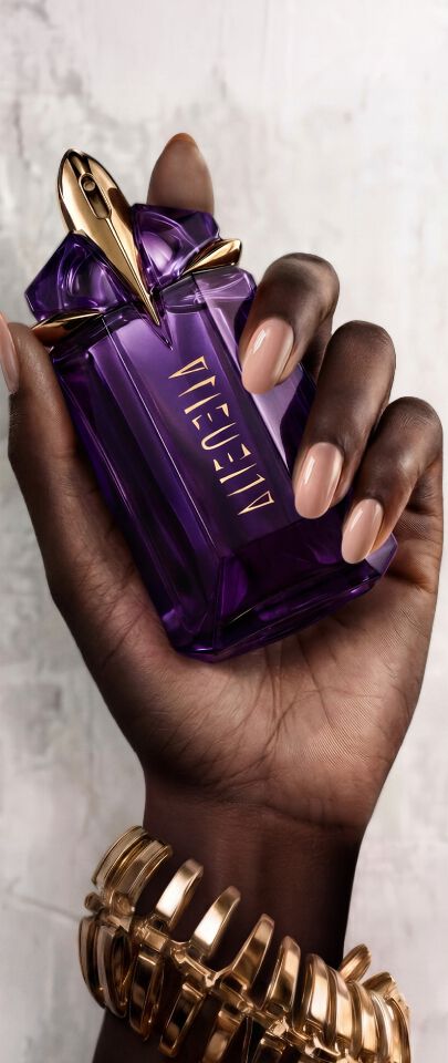 un flacon de parfum violet, un pot de creme violet et un flacon pompe alien sur un sol carrele avec une fleur bleu a cote