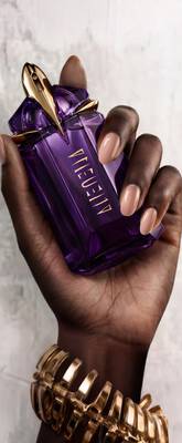 un flacon de parfum violet, un pot de creme violet et un flacon pompe alien sur un sol carrele avec une fleur bleu a cote