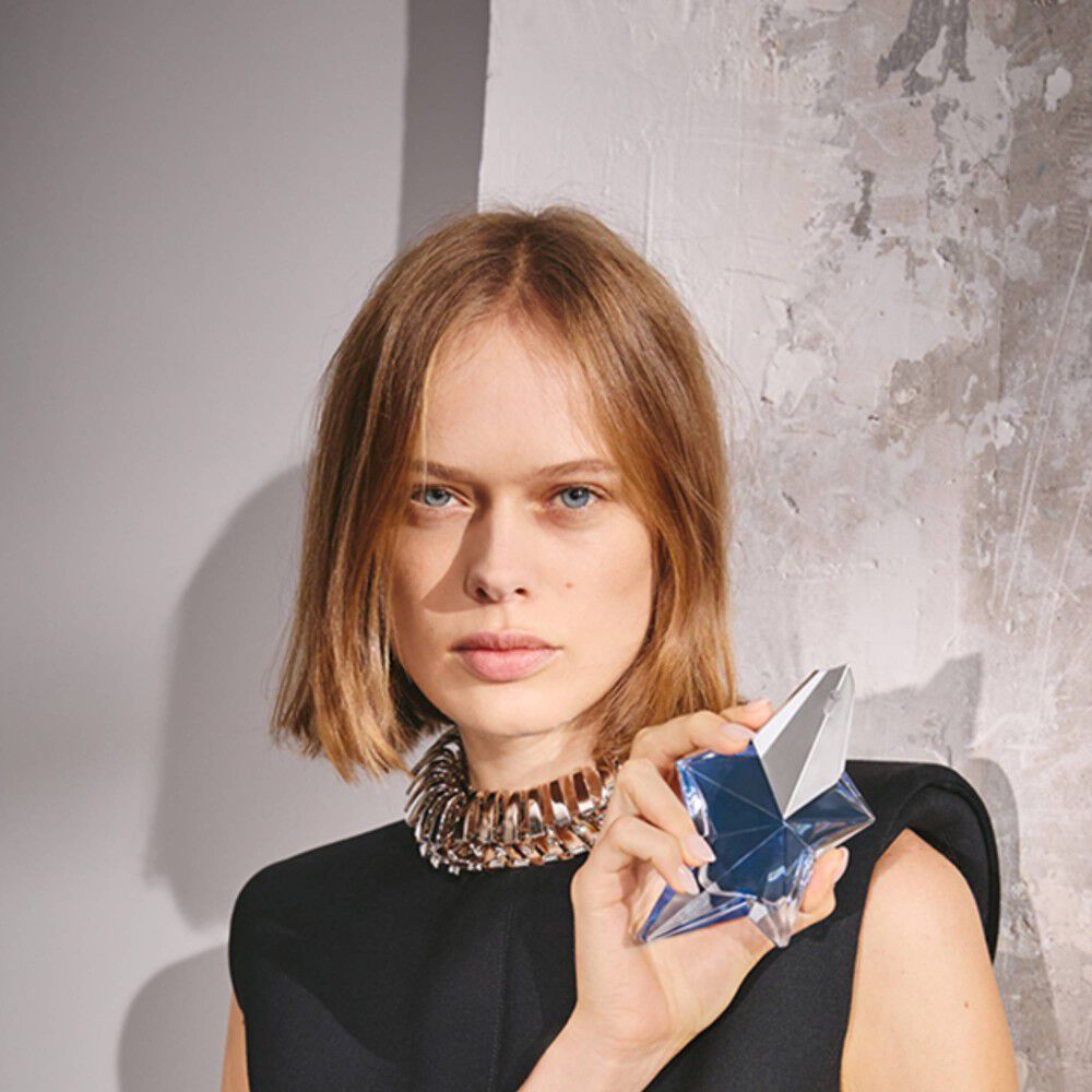une femme blonde tenant un flacon de parfum bleu en forme d'etoile