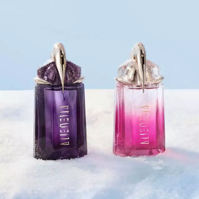 Deux flacons de parfum Mugler Alien, l'un d'un violet fonce classique (Alien eau de parfum) et l'autre d'un rose vif (Alien pulp), poses cote a cote sur une table de banquet recouverte de neige. Le texte indique « cadeaux a moins de 150 € ».