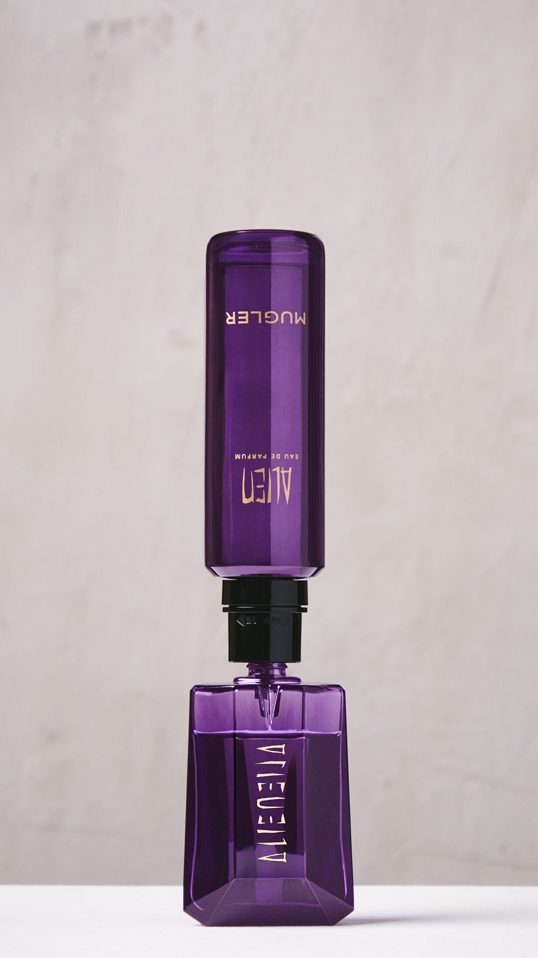 Une main en train de remplir le flacon violet de l'Eau de Parfum Alien a l'aide d'un flacon de recharge violet place a l'envers.