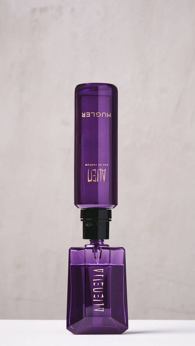 Une main en train de remplir le flacon violet de l'Eau de Parfum Alien a l'aide d'un flacon de recharge violet place a l'envers.