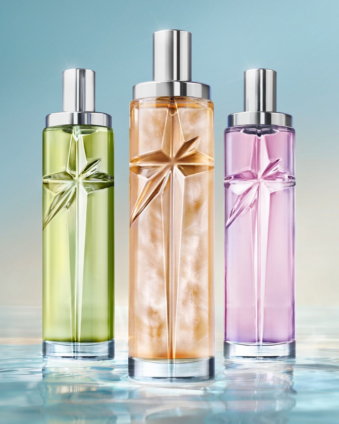Trois flacons des nouveaux eaux de toilette Starlicious, de couleur verte, orange et rose, flottant sur l'eau, sur fond bleu