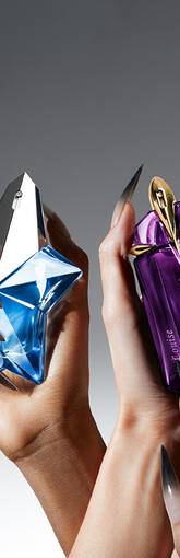 Deux mains feminines tenant des flacons de parfum futuristes, l'un bleu et l'autre violet, sur fond neutre.