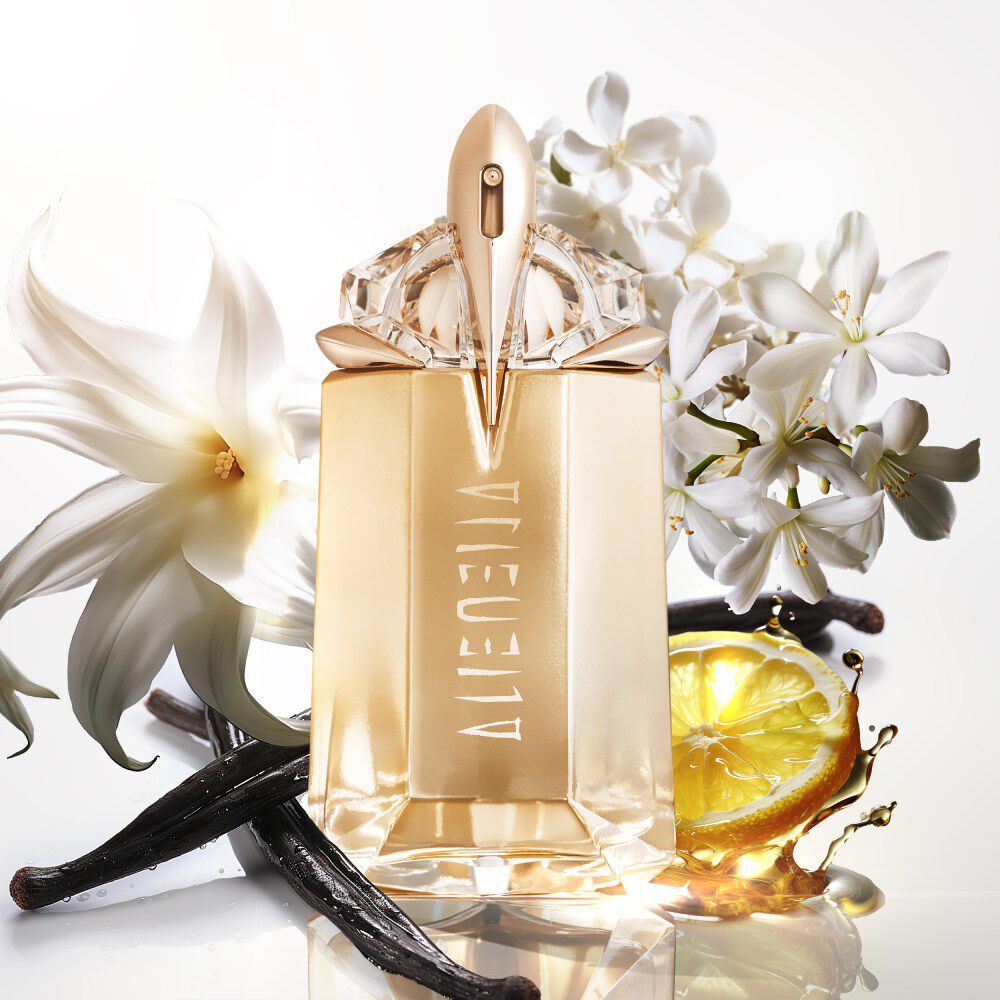 flacon de parfum dore alien mugler avec des fleurs de jasmin