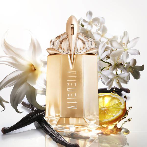 flacon de parfum dore alien mugler avec des fleurs de jasmin