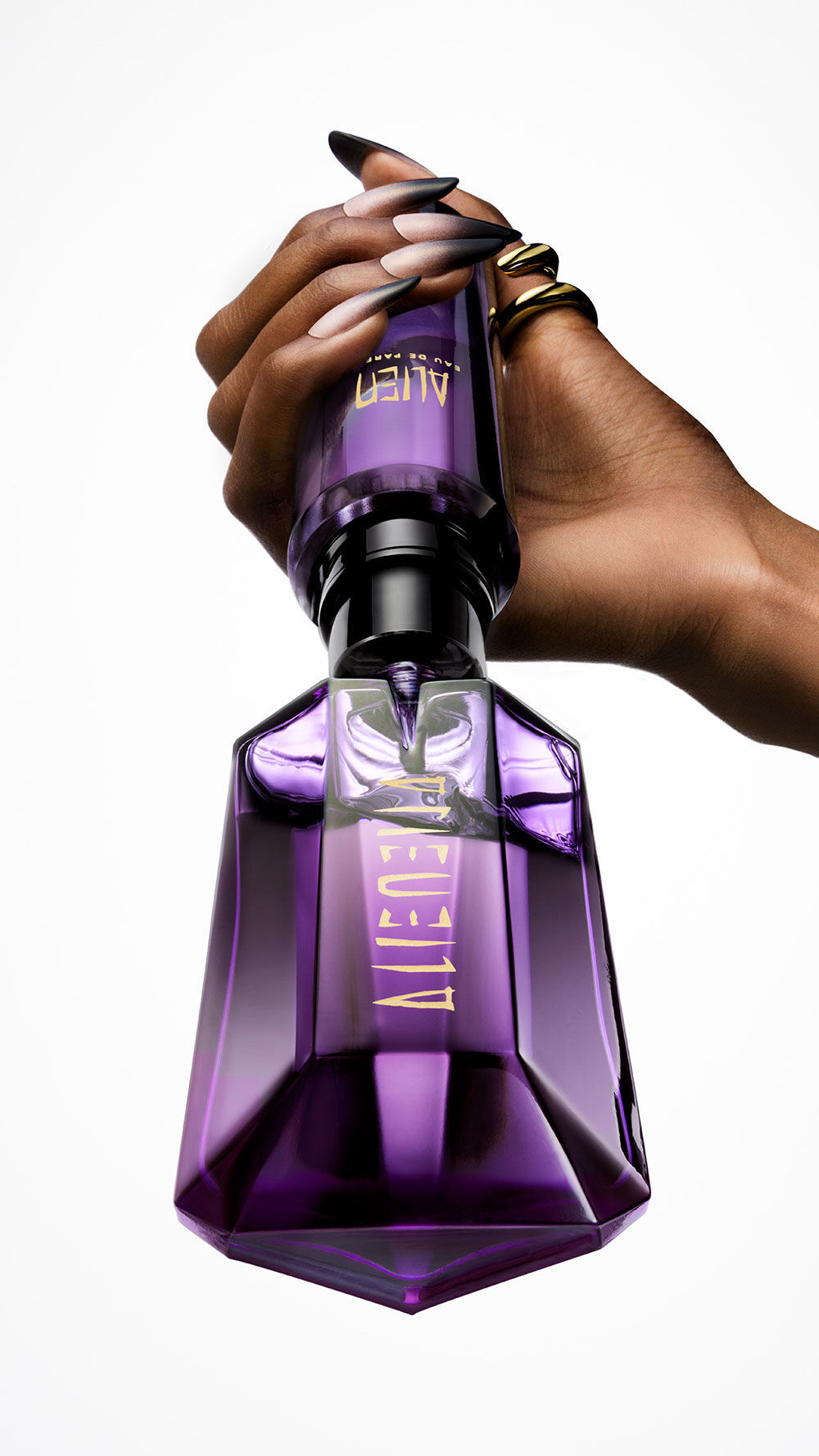 un flacon de parfum violet alien qui est rempli par une recharge tenue dans une main
