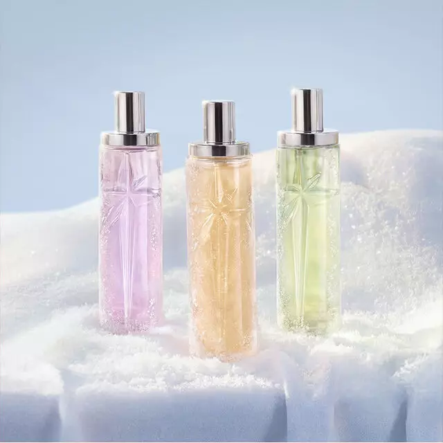 Trois grands flacons de parfum Mugler de forme cylindrique, aux teintes translucides de rose, d'orange et de vert clair, alignes debout dans la neige. La nouvelle collection Starlicious. Le texte indique « cadeaux a moins de 50€ ».
