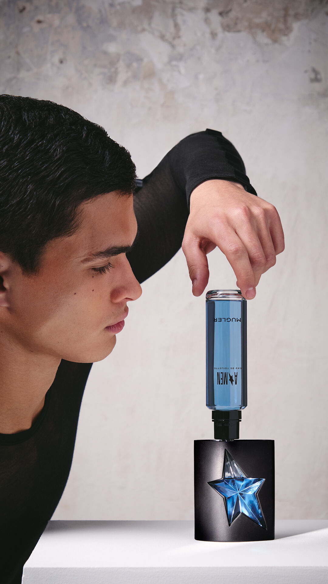 Une main en train de remplir le flacon noir et bleu de l'eau de toilette A*Men « Star » a l'aide d'un flacon de recharge bleu place a l'envers.