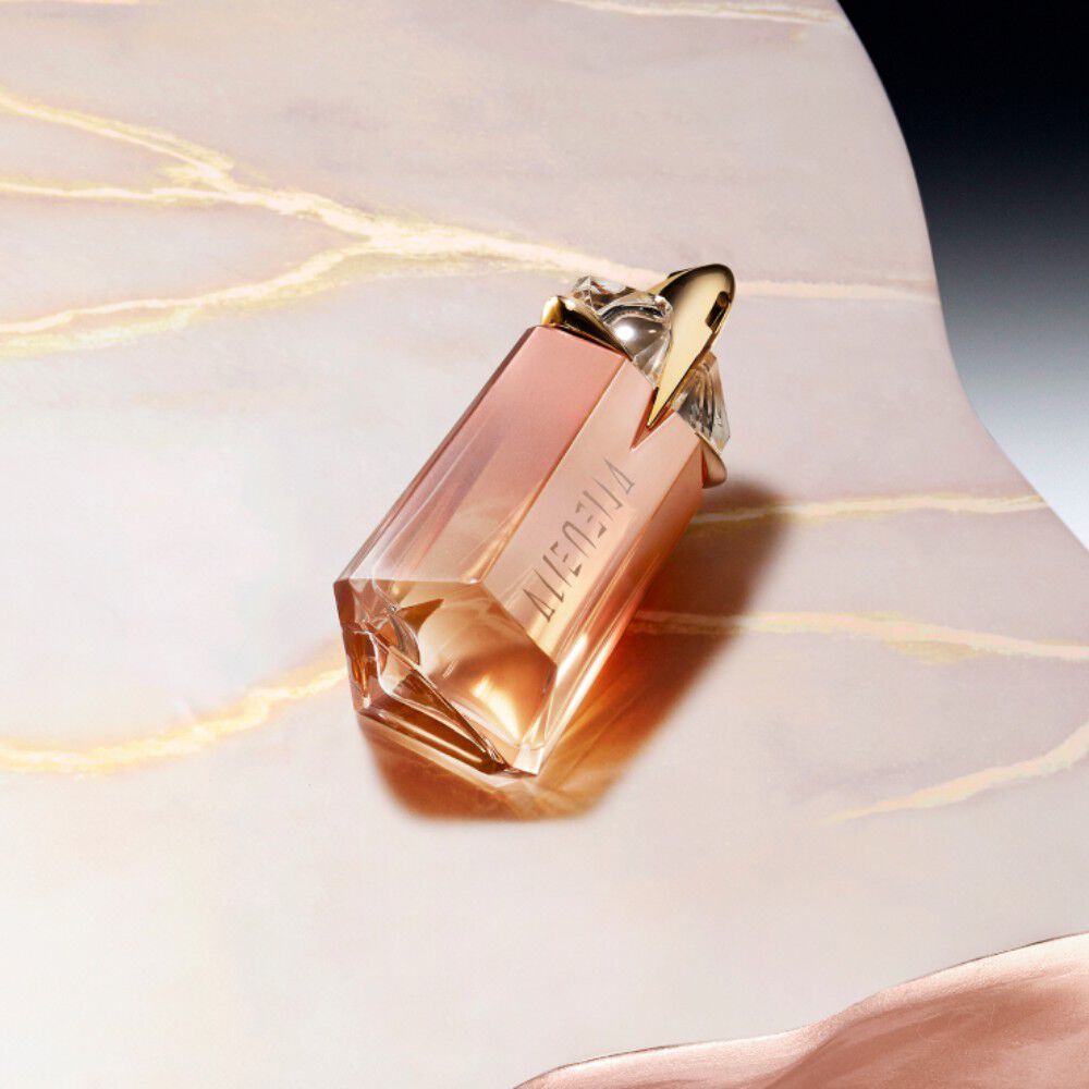 Flacon de parfum en forme de diamant, aux teintes rose et dore, sur une surface marbree.