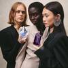Trois femmes tiennent des flacons de parfum bleu et violet. Le fond est un mur beige