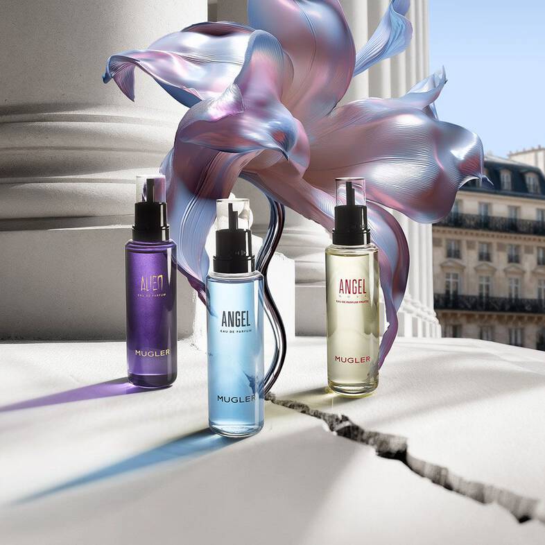 trois flacons recharges de parfums bleu, violet et jaune sur un sol carrele a cote d'une fleur bleu