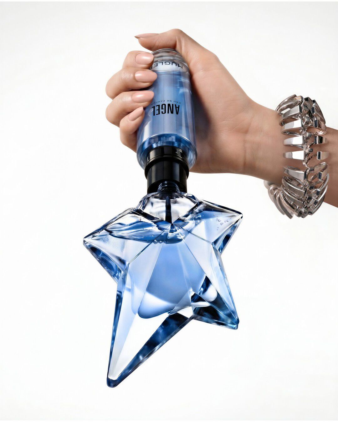 Une main tenant le flacon classique bleu en forme d'etoile de l'Eau de Parfum Angel, oriente vers le haut, sur un fond blanc uni.