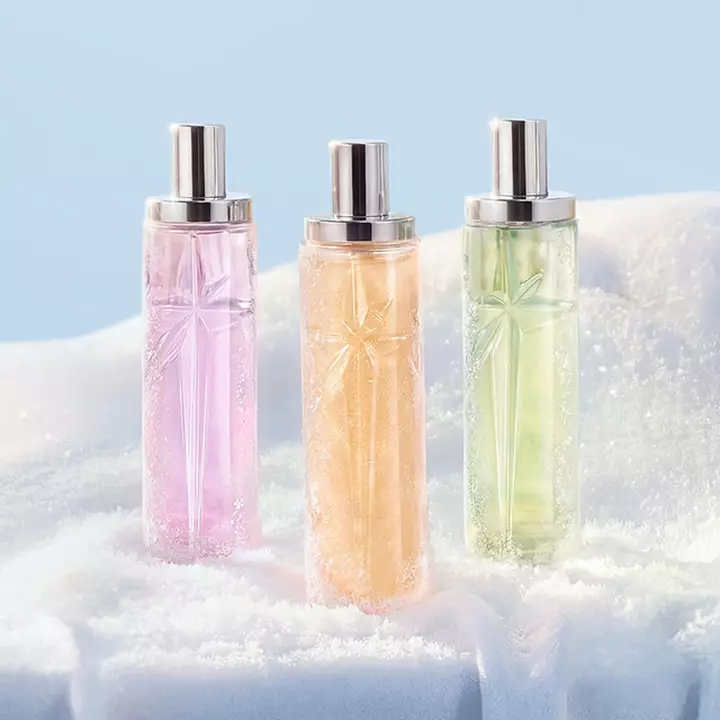 un flacon de parfum rose, orange et vert poses dans de la neige blanche
