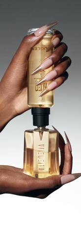 Deux mains elegantes tiennent une bouteille de parfum doree, mettant en avant des ongles longs et stylises.