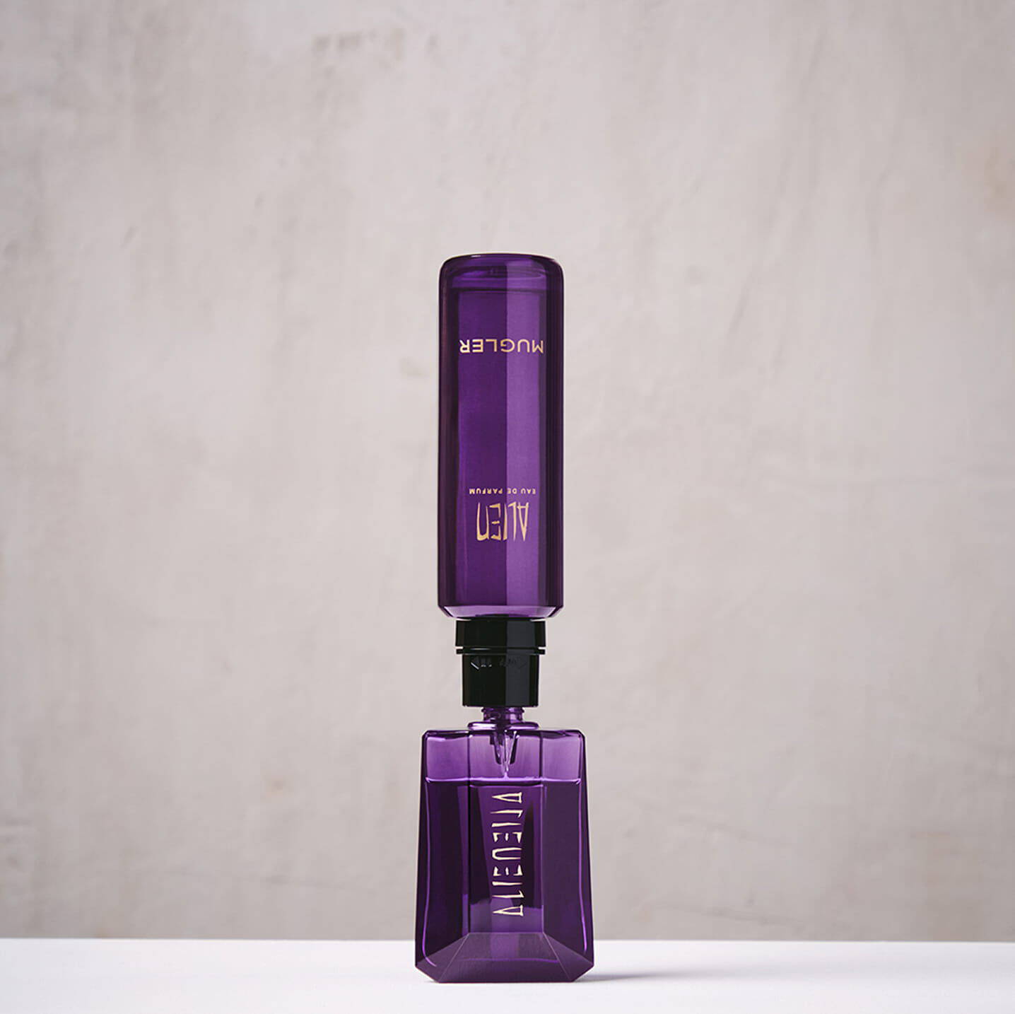 Flacon rechargeable d'eau de parfum « Alien » de Mugler, de couleur violette, place a la verticale pour le service « Mugler Fountain ».