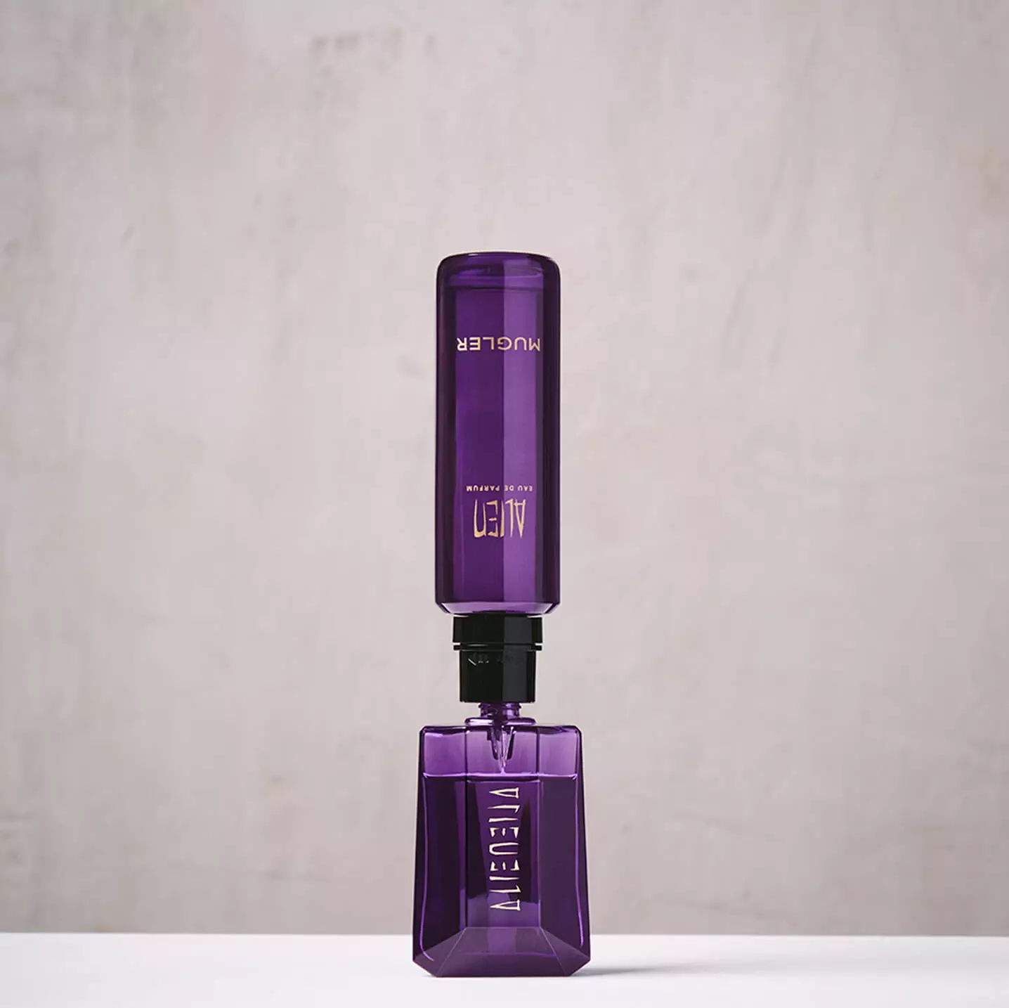 Flacon rechargeable d'eau de parfum « Alien » de Mugler, de couleur violette, place a la verticale pour le service « Mugler Fountain ».