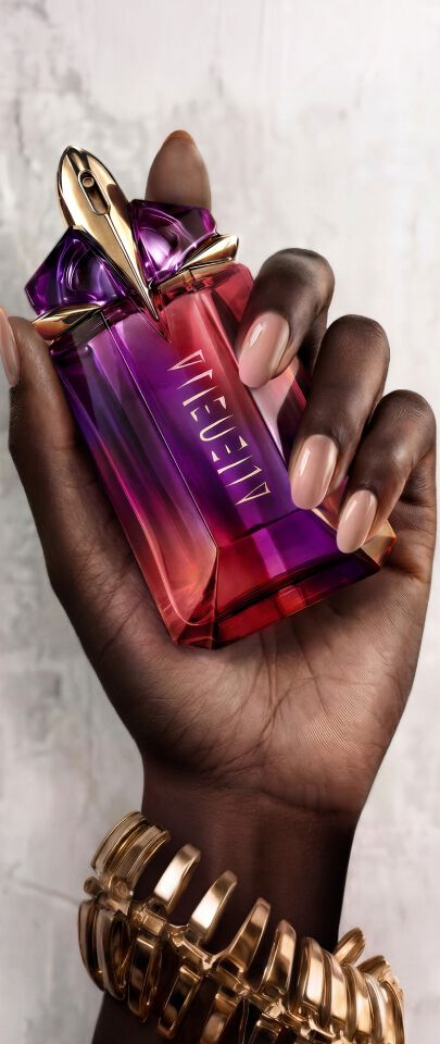 Main dans la main, deux flacons de parfum Mugler, l’un violet, l’autre rouge, sont en train d'etre assembles.