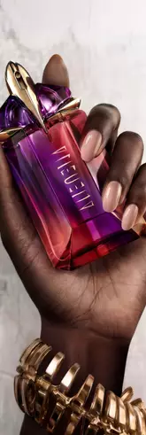 Main dans la main, deux flacons de parfum Mugler, l’un violet, l’autre rouge, sont en train d'etre assembles.