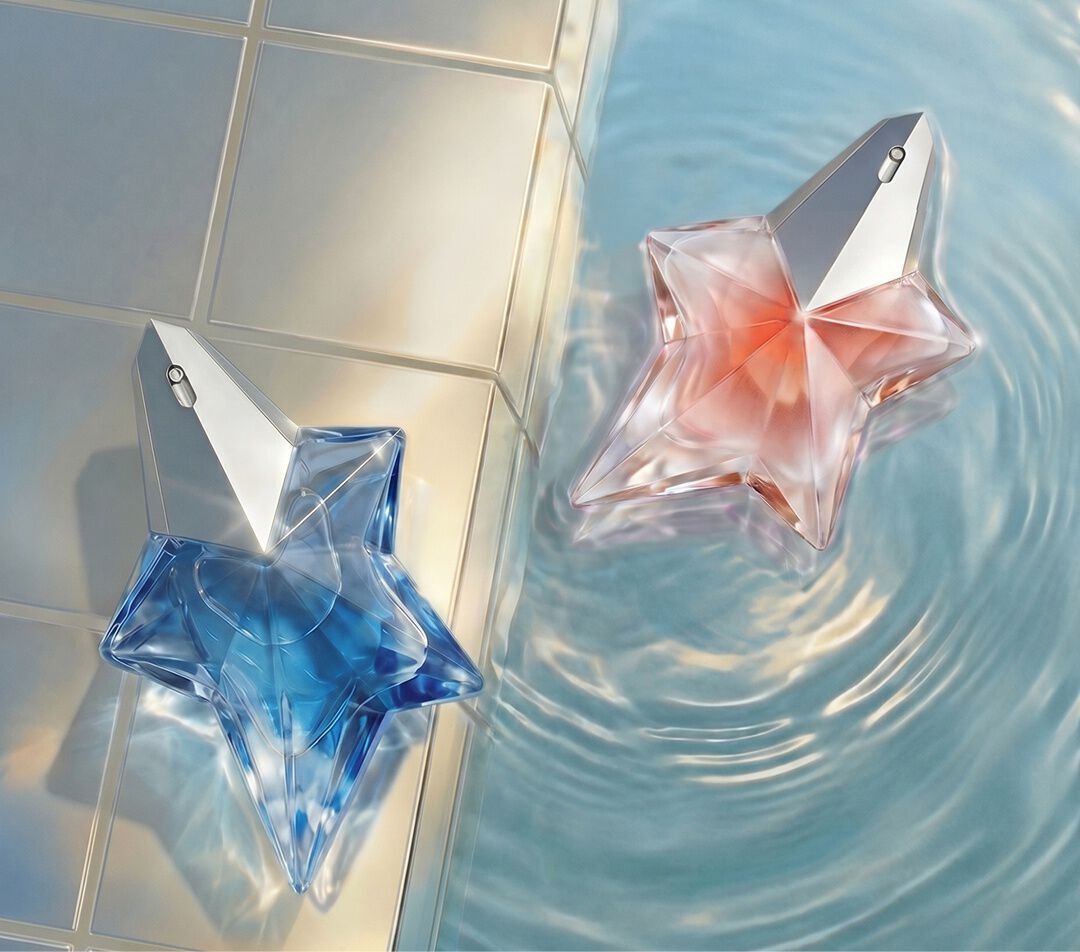 Des flacons de parfum en forme d'etoile, aux teintes bleu et rose pale, de la ligne « Angel » d'Anna S. Mugler (eau de parfum et blush), flottent dans une eau limpide et ondulante, pres d'un rebord carrele aux reflets irises.