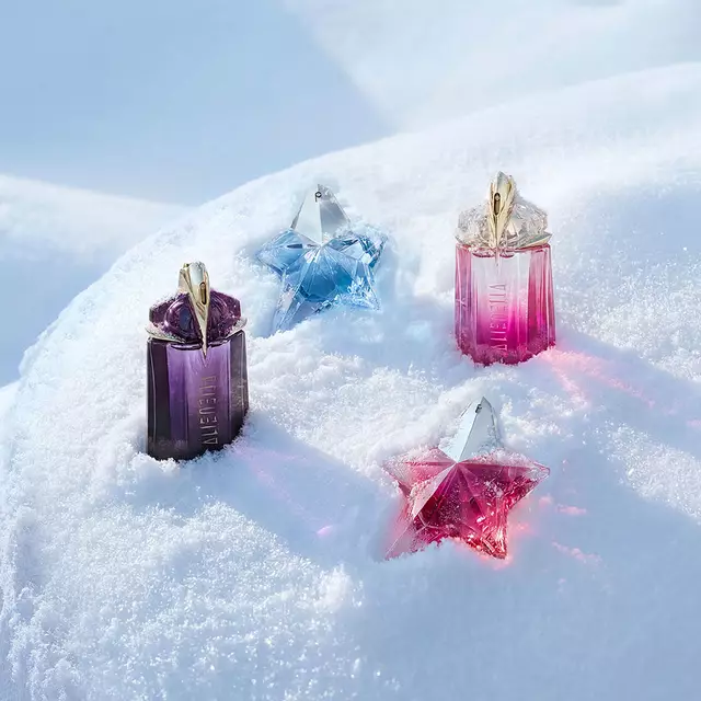 Un flacon violet d'Alien de Mugler, un flacon bleu clair d'Angel, un flacon rose d'Alien et un flacon rose d'Angel, magnifiquement disposes sur une surface de neige douce et ondulee. L'image redirige vers notre guide cadeaux.