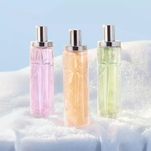 un flacon de parfum rose, orange et vert poses dans de la neige blanche