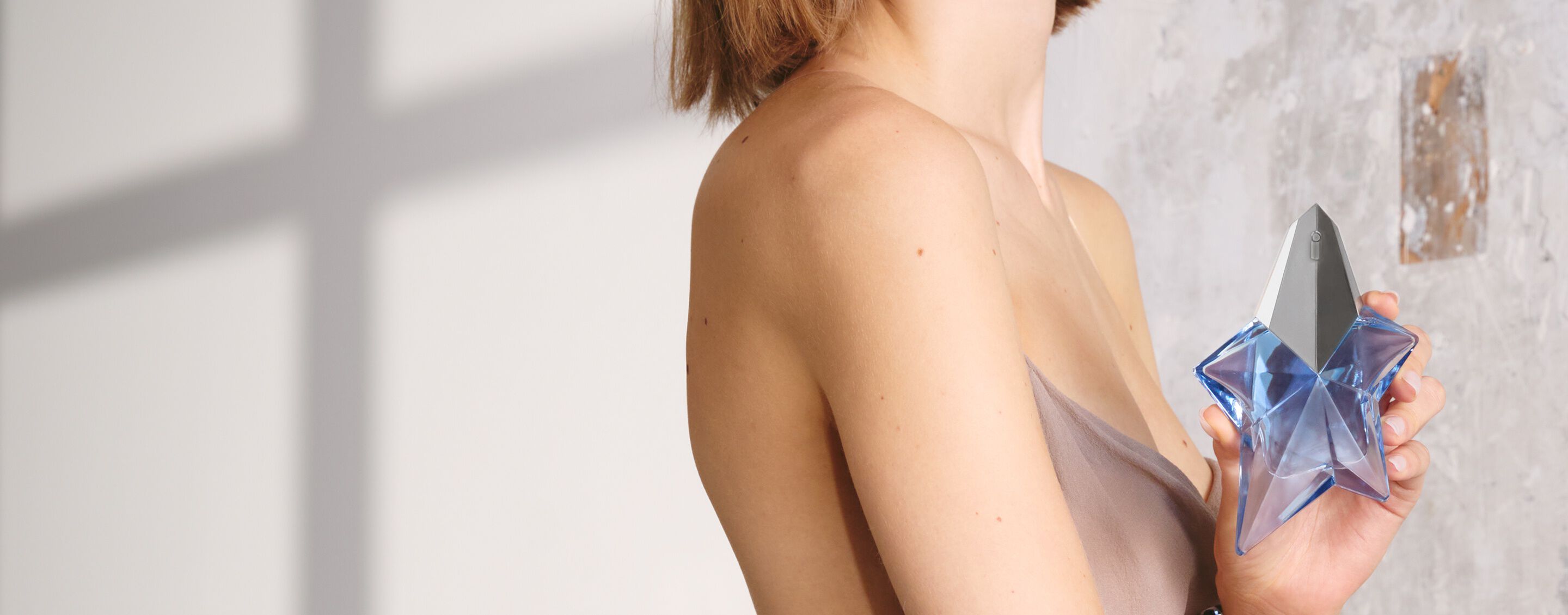 le buste d'une femme tenant dans sa main un flacon de parfum bleu en forme d'étoile sur un fond beige