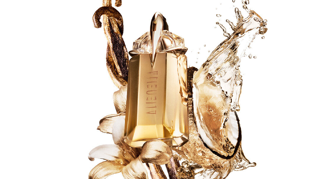 un flacon de parfum doré mugler entouré d'une noix de coco, d'une fleur de jasmin et de morceau de vanille