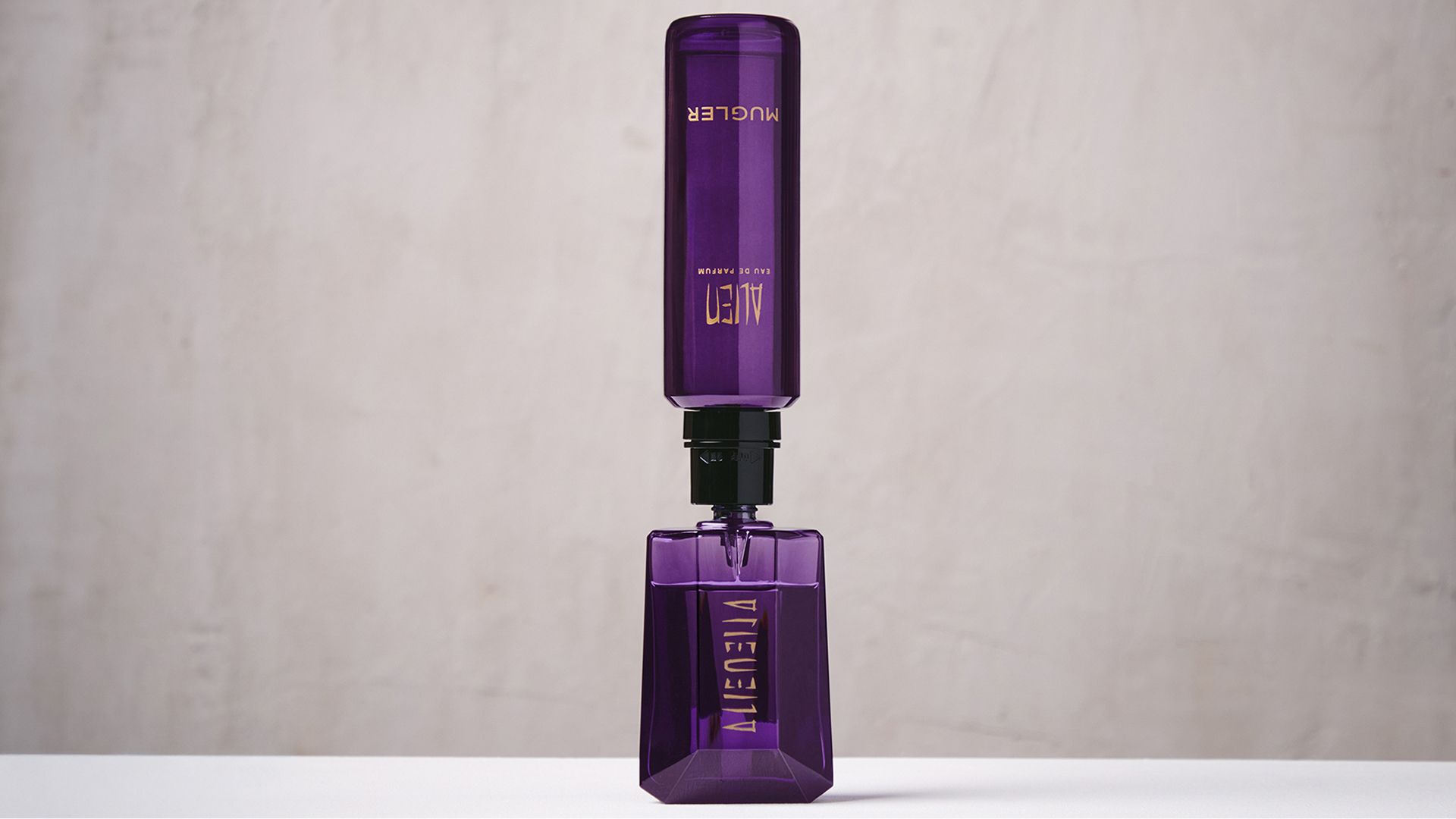 un flacon de parfum violet remplit par une recharge violet sur un fond beige