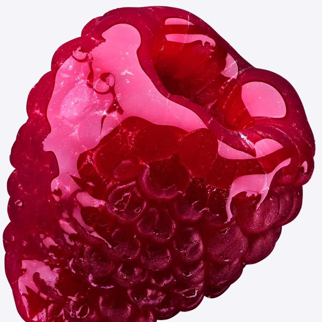 Gros plan extrême d une framboise recouverte d un liquide translucide rouge foncé et brillant, sur un fond clair