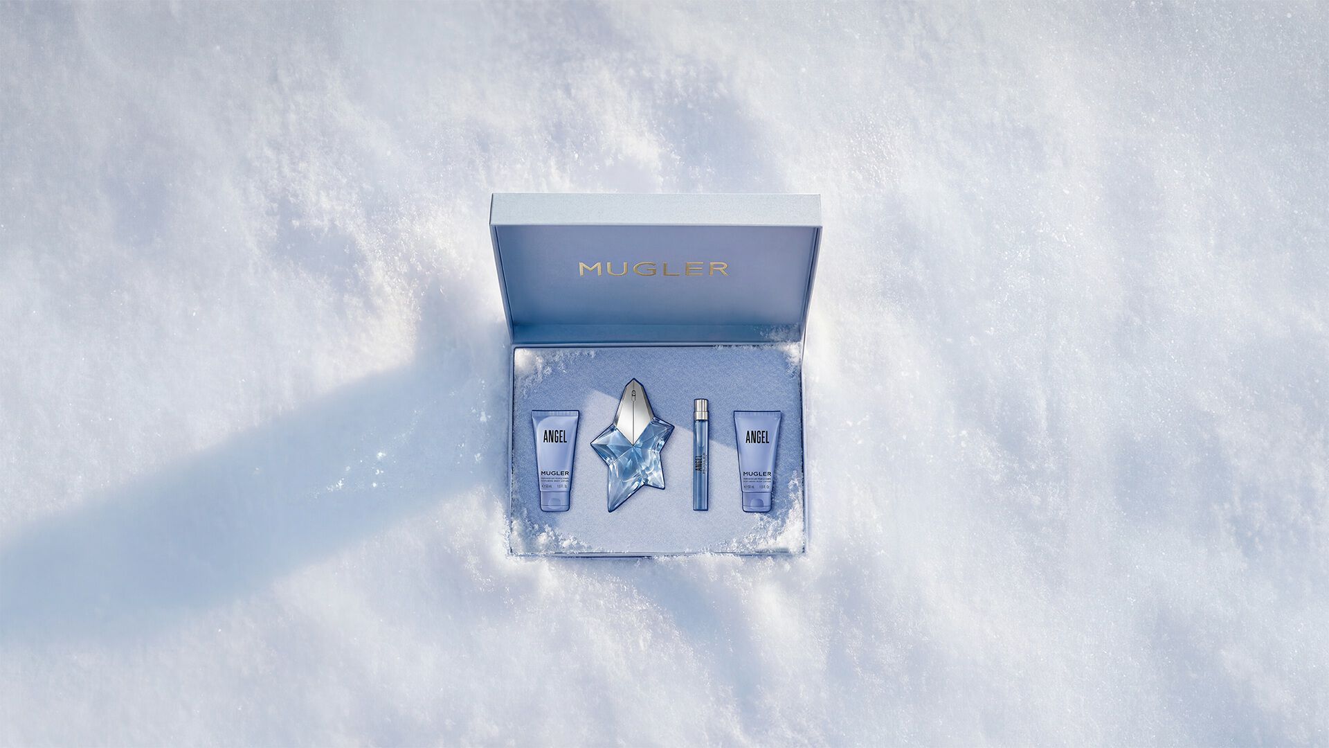 Un coffret cadeau Mugler bleu glacier, ouvert, texturé et scintillant, posé sur de la neige, dévoilant un coffret cadeau de luxe contenant l eau de parfum Angel de 50 ml