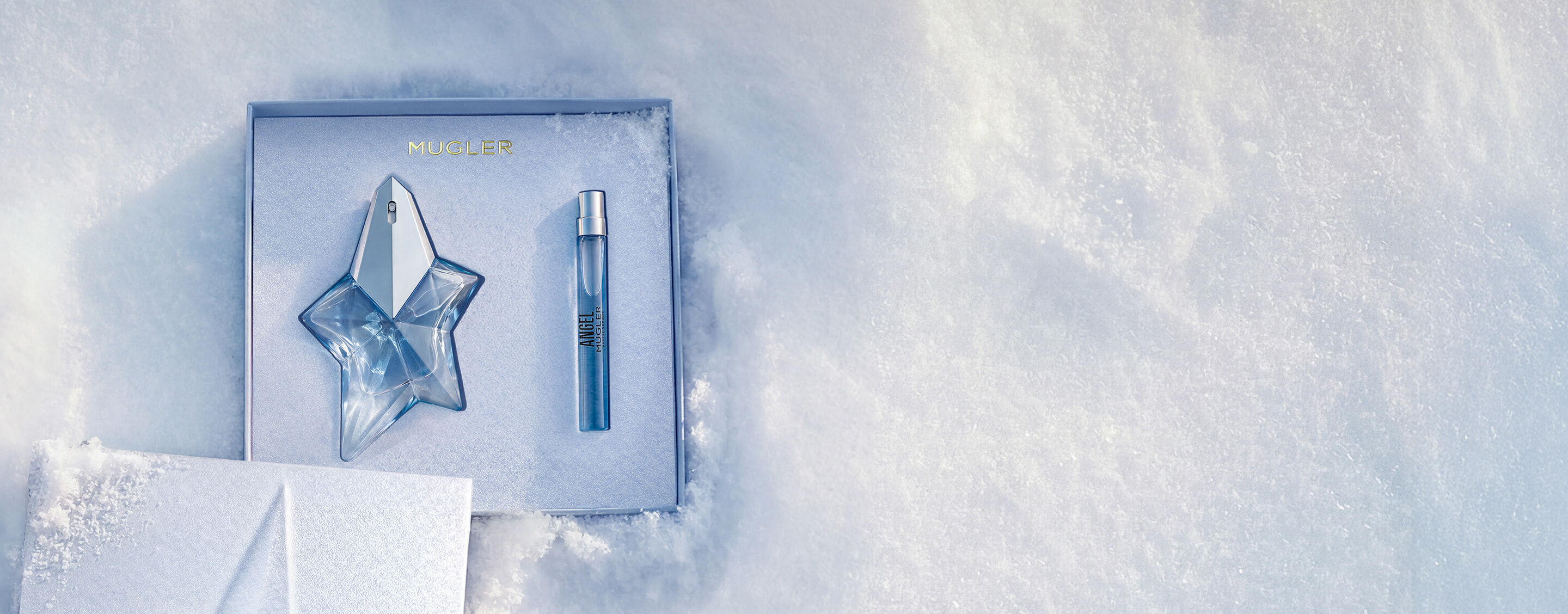 Un coffret cadeau Mugler bleu glacier, ouvert, texturé et scintillant, posé sur de la neige, dévoilant un coffret cadeau Angel eau de parfum 25 ml