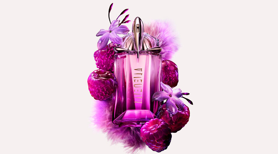 Flacon de parfum rose mugler entourée de framboises fraîches sur un fond neutre.