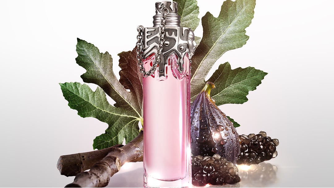 un flacon de parfum rose pâle entouré de figues et de feuilles vertes