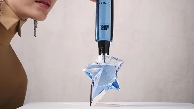 une femme en train de remplir un flacon d'Angel de Mugler