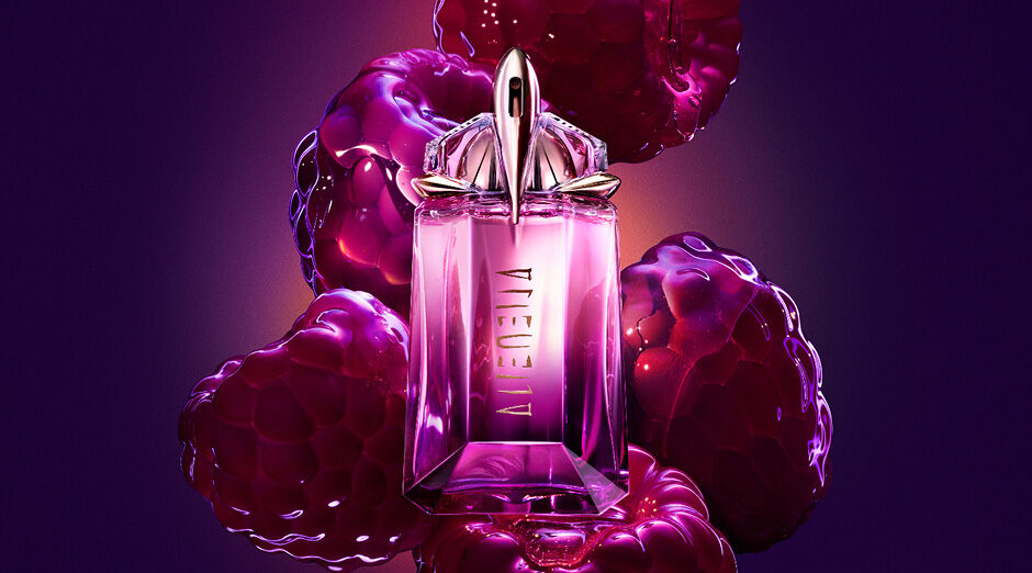 Flacon de parfum rose mugler entourée de framboises fraîches sur un fond neutre.