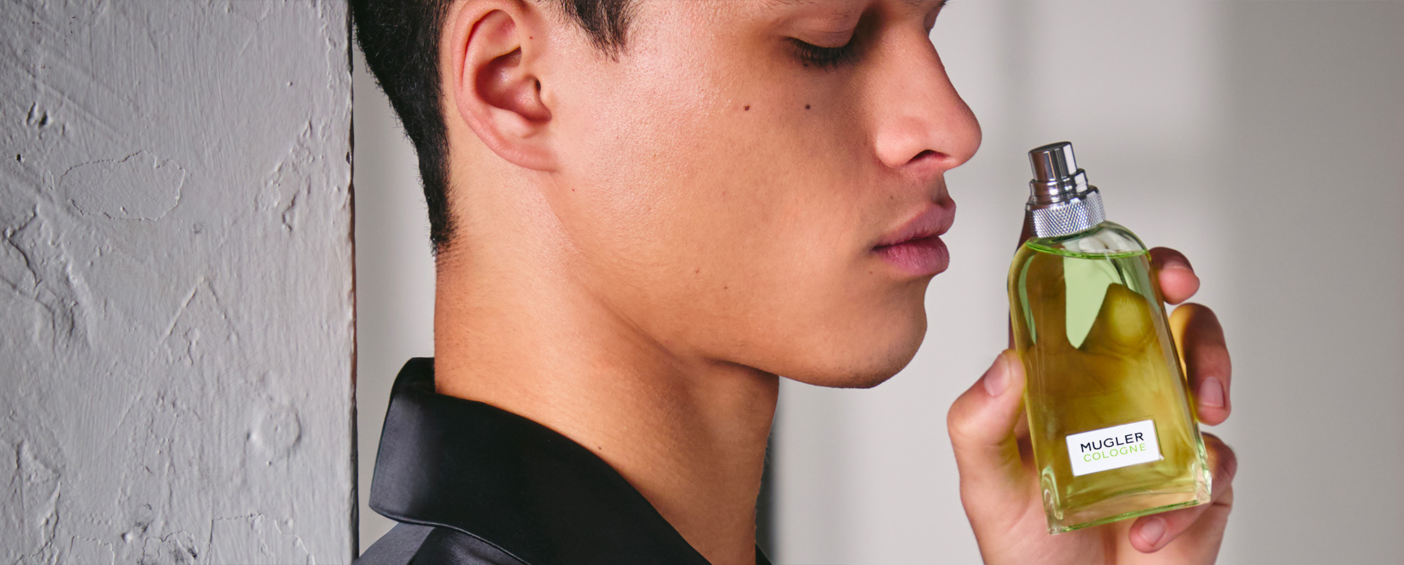 Un homme vu de profil, les yeux fermés, montre un flacon d'eau de Cologne Mugler qu'il tient entre ses mains.