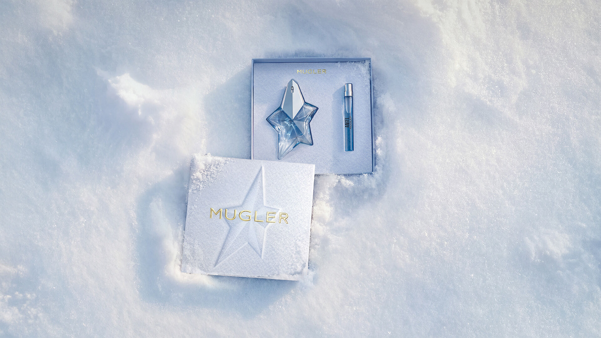 Un coffret cadeau Mugler bleu glacier, ouvert, texturé et scintillant, posé sur de la neige, dévoilant un coffret cadeau Angel eau de parfum 25 ml