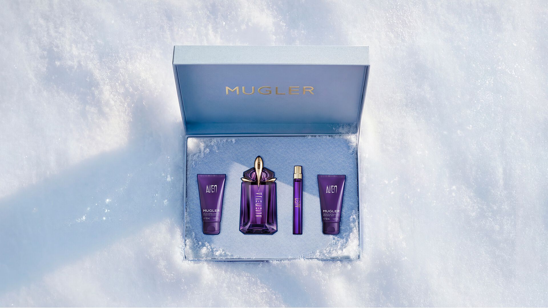 Un coffret cadeau Mugler bleu glacier, ouvert, texturé et scintillant, posé sur de la neige, dévoilant un coffret cadeau de luxe contenant une eau de parfum Alien de 60 ml