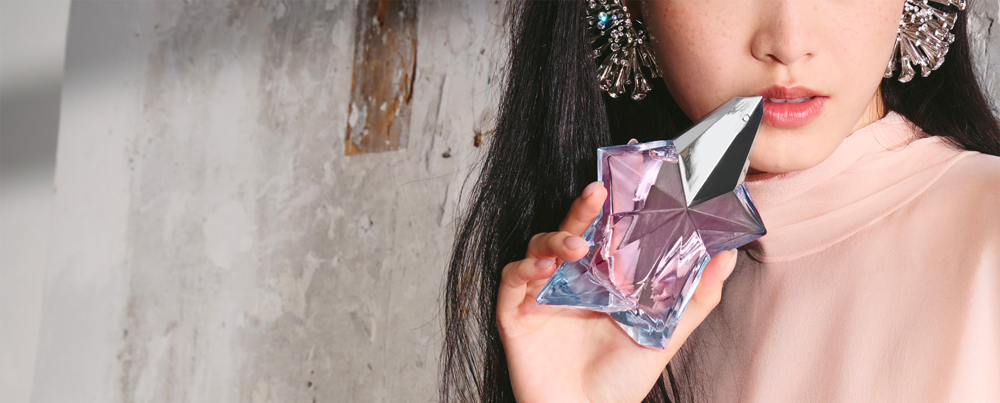 Photo de style de vie mettant en scène une femme tenant le flacon transparent rose pâle en forme d'étoile de l'eau de toilette Mugler Angel, un parfum frais et féminin