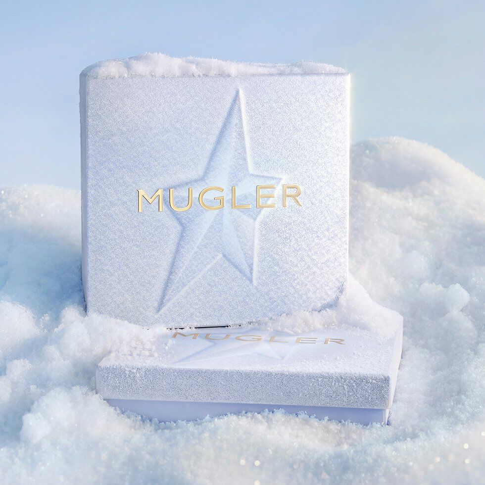 Un coffret cadeau Mugler unique, de couleur bleu clair texturé et orné d'un motif d'étoiles en relief, se détache magnifiquement sur une congère douce baignée de soleil.