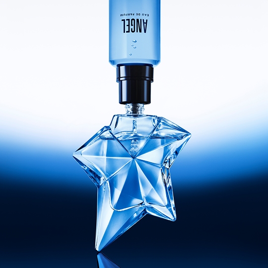Flacon de parfum en forme d'étoile, couleur bleu, avec un bouchon noir. Éclat brillant sur fond dégradé.