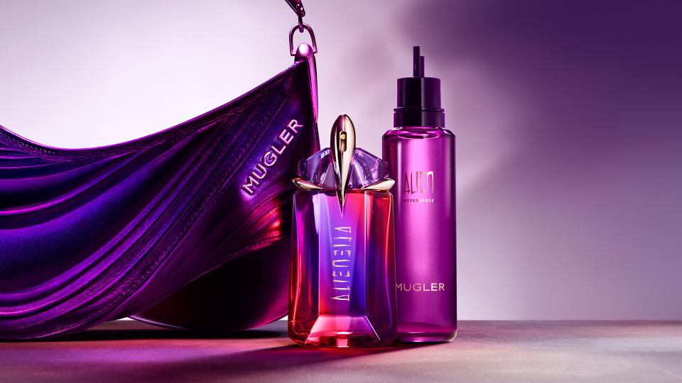 Flacon de parfum Alien de Mugler, accompagné d'un vaporisateur, le tout sur un fond violet élégant.