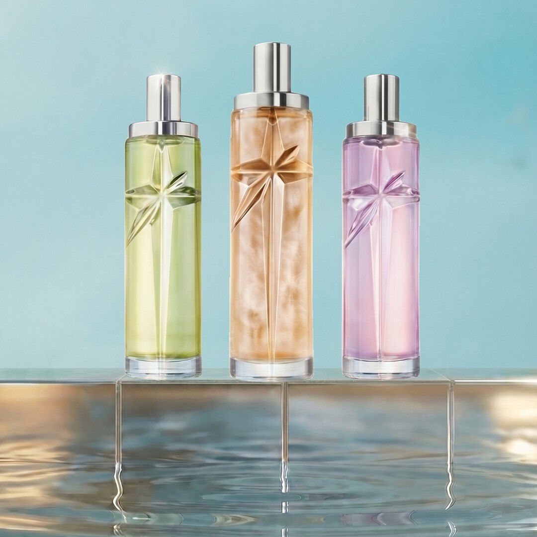 Trois flacons de recharge Mugler Starlicious, de couleur verte, ambrée et rose pâle, présentés sur le rebord carrelé d une piscine, sur un fond bleu lumineux.