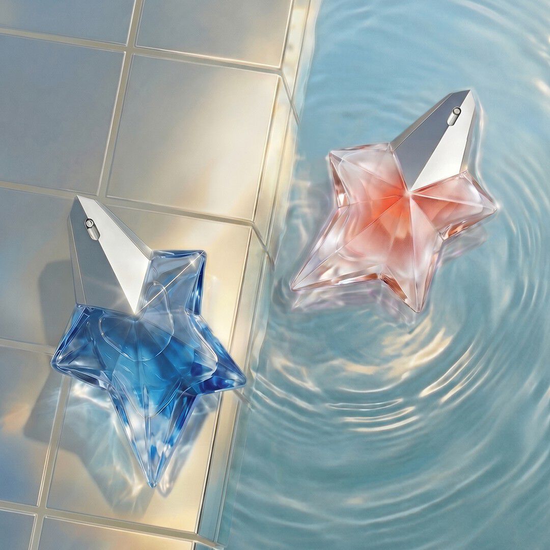 Les flacons en forme d étoile de Mugler Angel Eau de Parfum et Angel Blush, bleus et rose pâle, flottent dans une eau limpide et ondulante, près d un rebord carrelé aux reflets irisés.