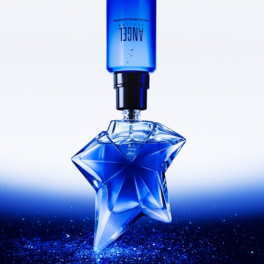 Flacon de parfum en forme d'étoile, de couleur bleu, avec une bouteille au-dessus, sur fond dégradé.