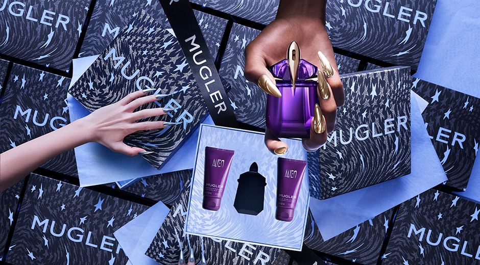 Main image d'un parfum Mugler avec des produits associés et des boîtes décoratives, sur un fond coloré et texturé.