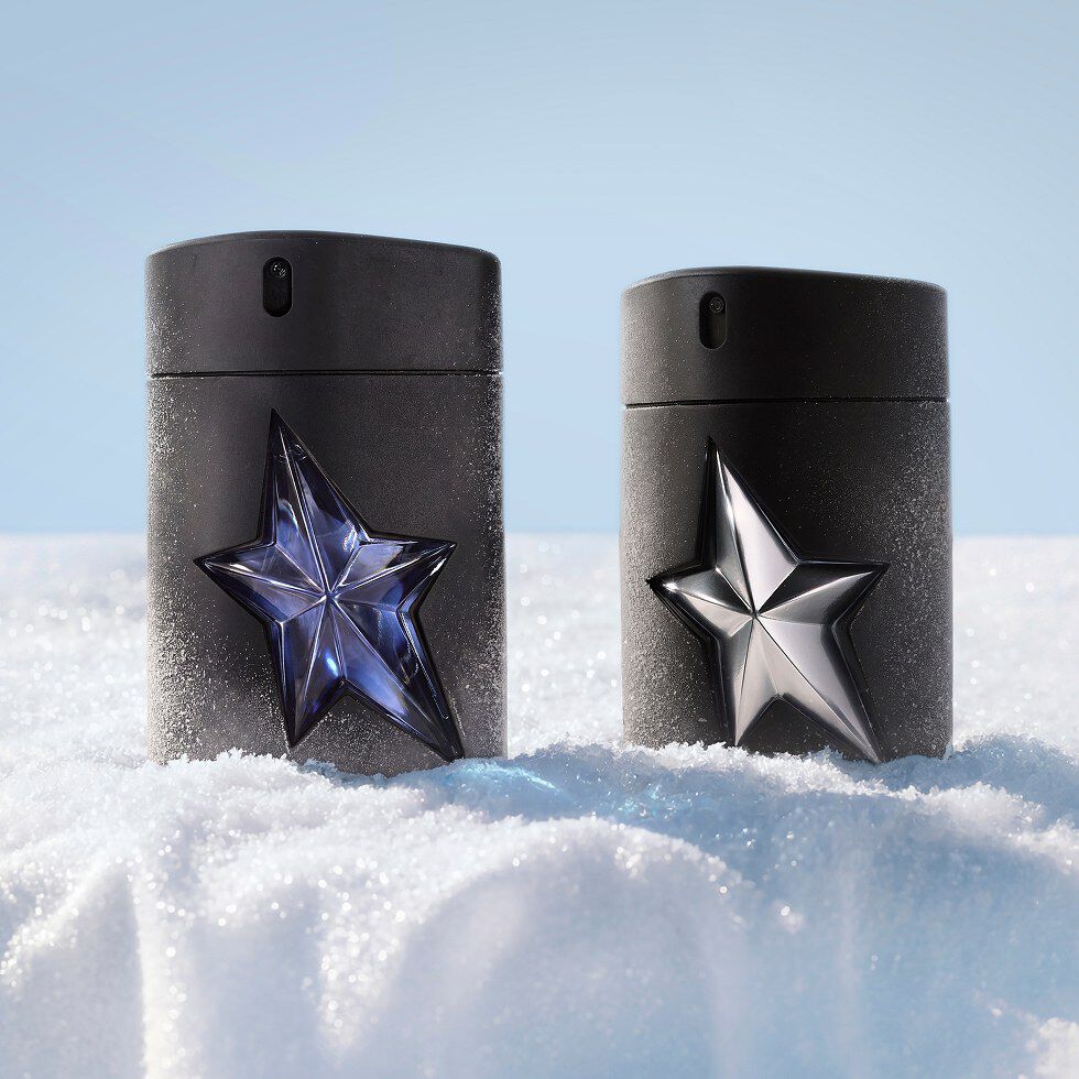 Deux flacons noirs de Mugler A*Men posés côte à côte dans la neige, l un orné d une étoile bleue (Eau de Toulette) et l autre d une étoile argentée métallisée (Fantasm).