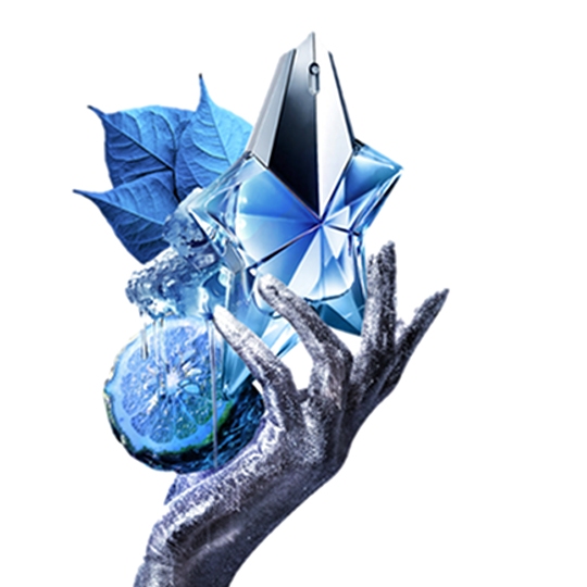 Flacon de parfum en forme d'étoile bleu, tenu par une main argentée, avec des feuilles et des agrumes en arrière-plan.